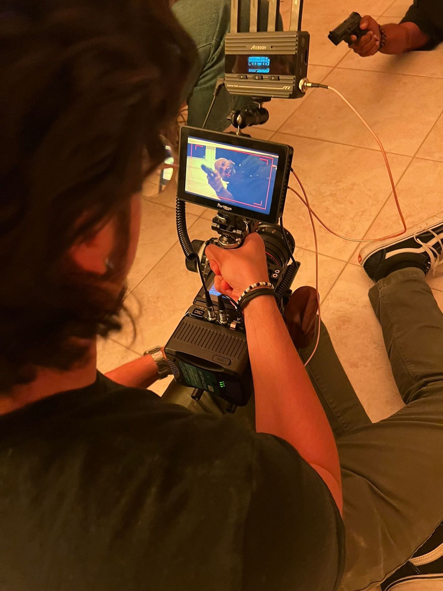 Person holding a camera with a monitor displaying a scene being filmed on a tiled floor.